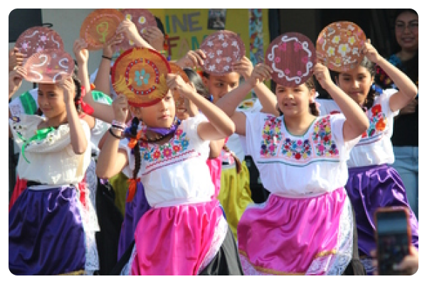Four students wear traditional colorful costumes holding up homemade artwork.